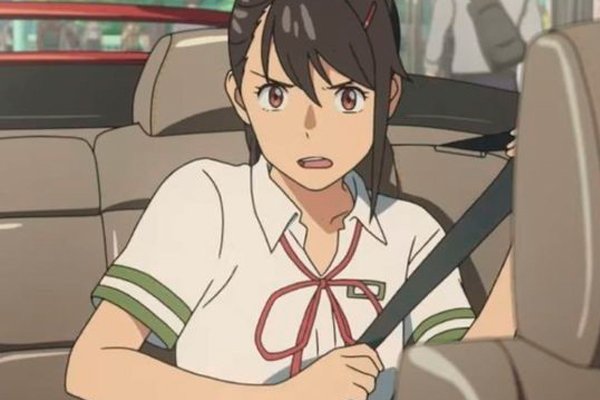 Suzume se encuentra en el auto del amigo de Souta, con su cinturón de seguridad abrochado y luciendo su uniforme de colegio, preparada para enfrentar lo que le depara el viaje en la película Suzume.